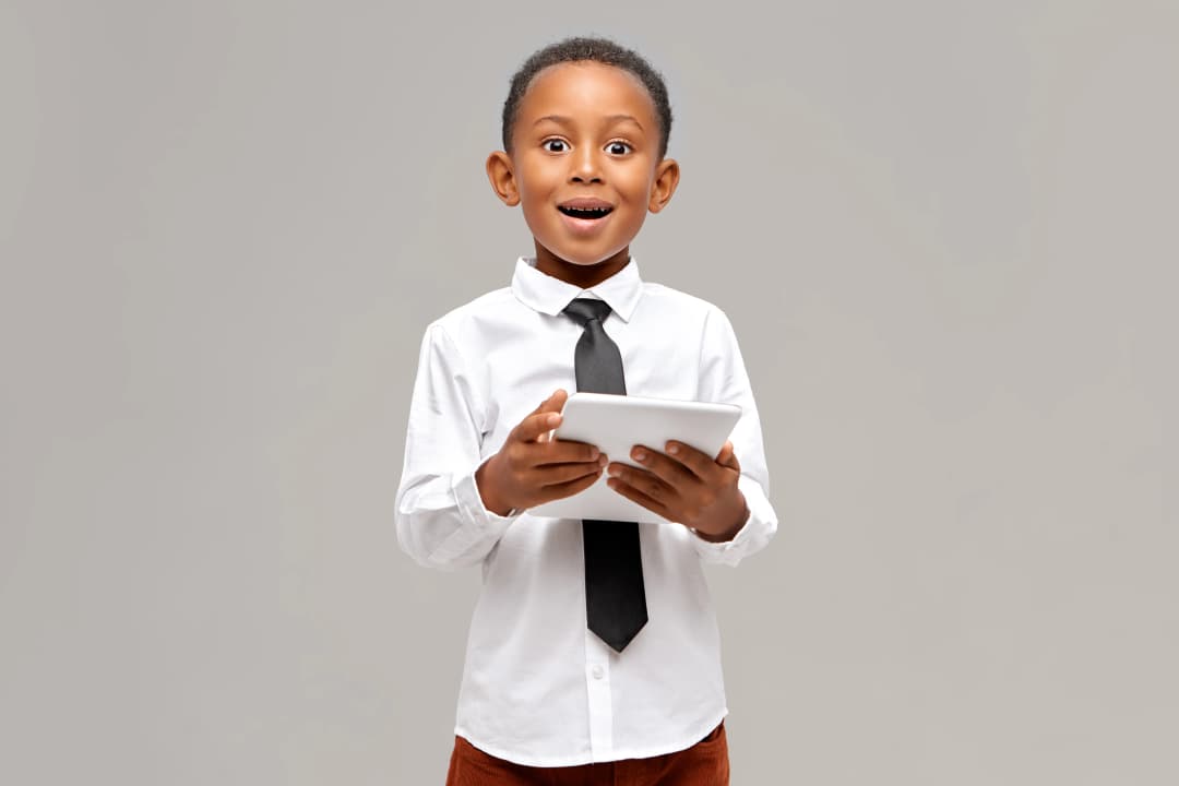 Giant Strides EduTech Consulting Limited-astonished dark skinned little boy wearing white shirt black tie enjoying high speed wireless internet connection digital tablet having surprised amazed look watching cartoon online